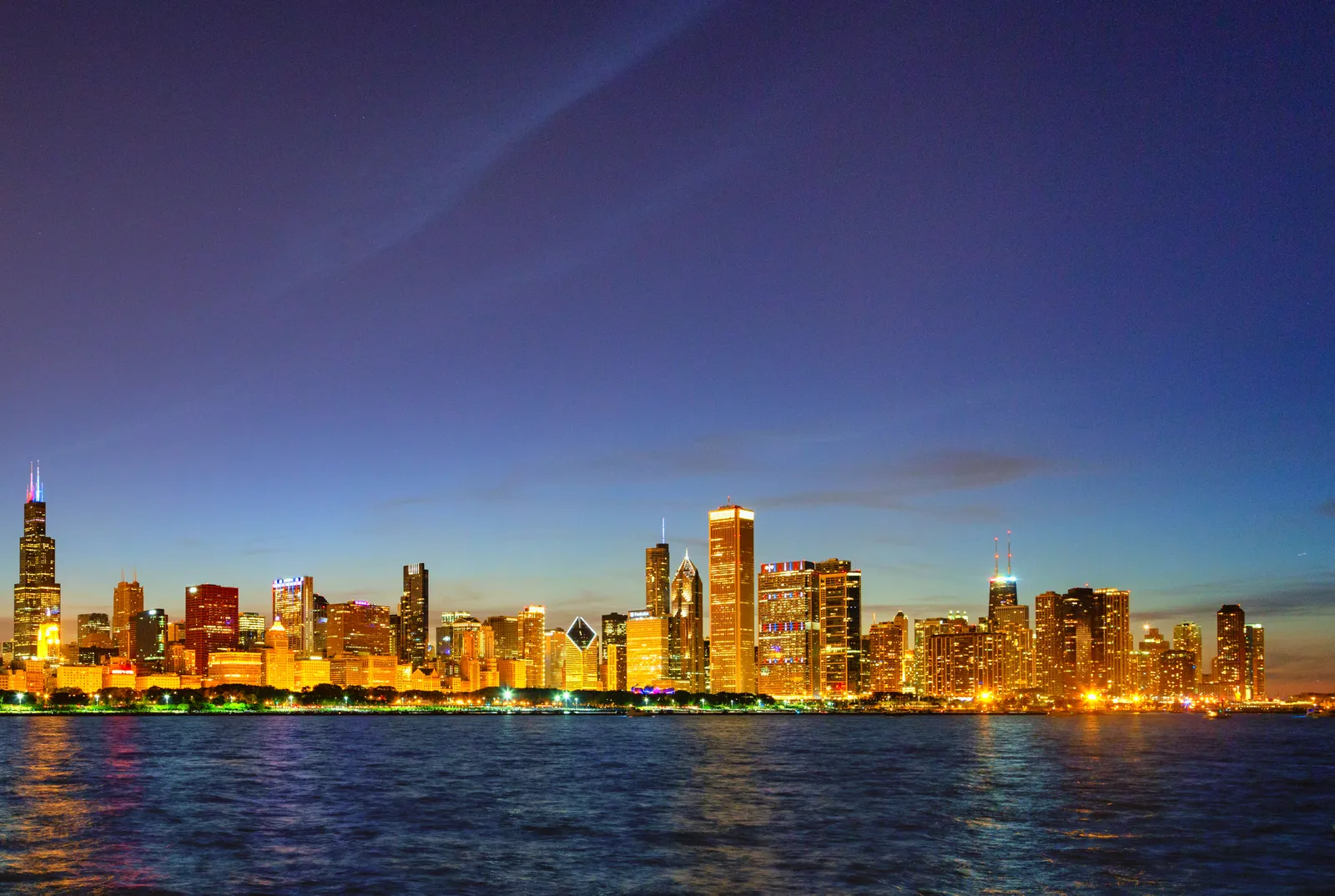 The Chicago skyline lit up at dusk, viewed across Lake Michigan