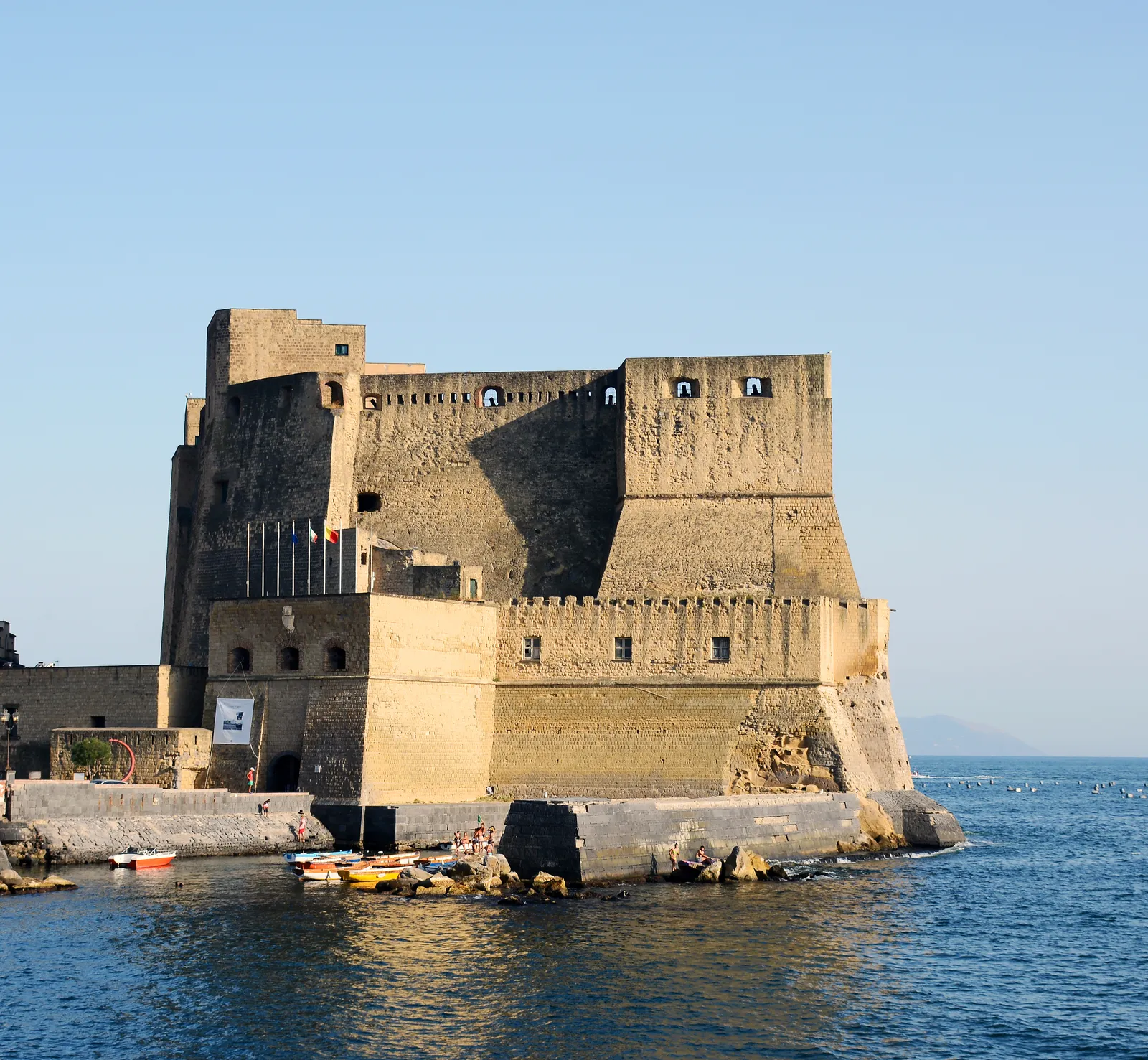 Castel dell'Ovo, a stone castle on a small island connected to the Naples waterfront, with fishing boats moored below