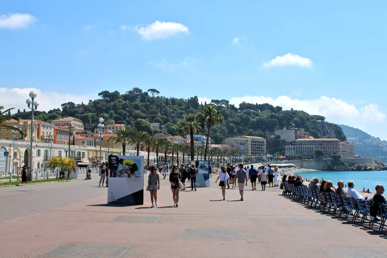 Palm-lined Promenade des Anglais in Nice on a sunny day, with the hillside and coastline curving into the distance
