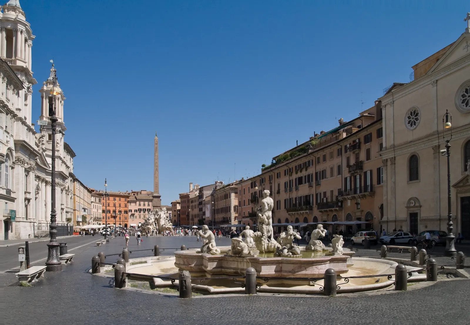 Piazza Navona in Rome, a long open square with a central fountain, obelisk, and surrounding buildings under a clear sky