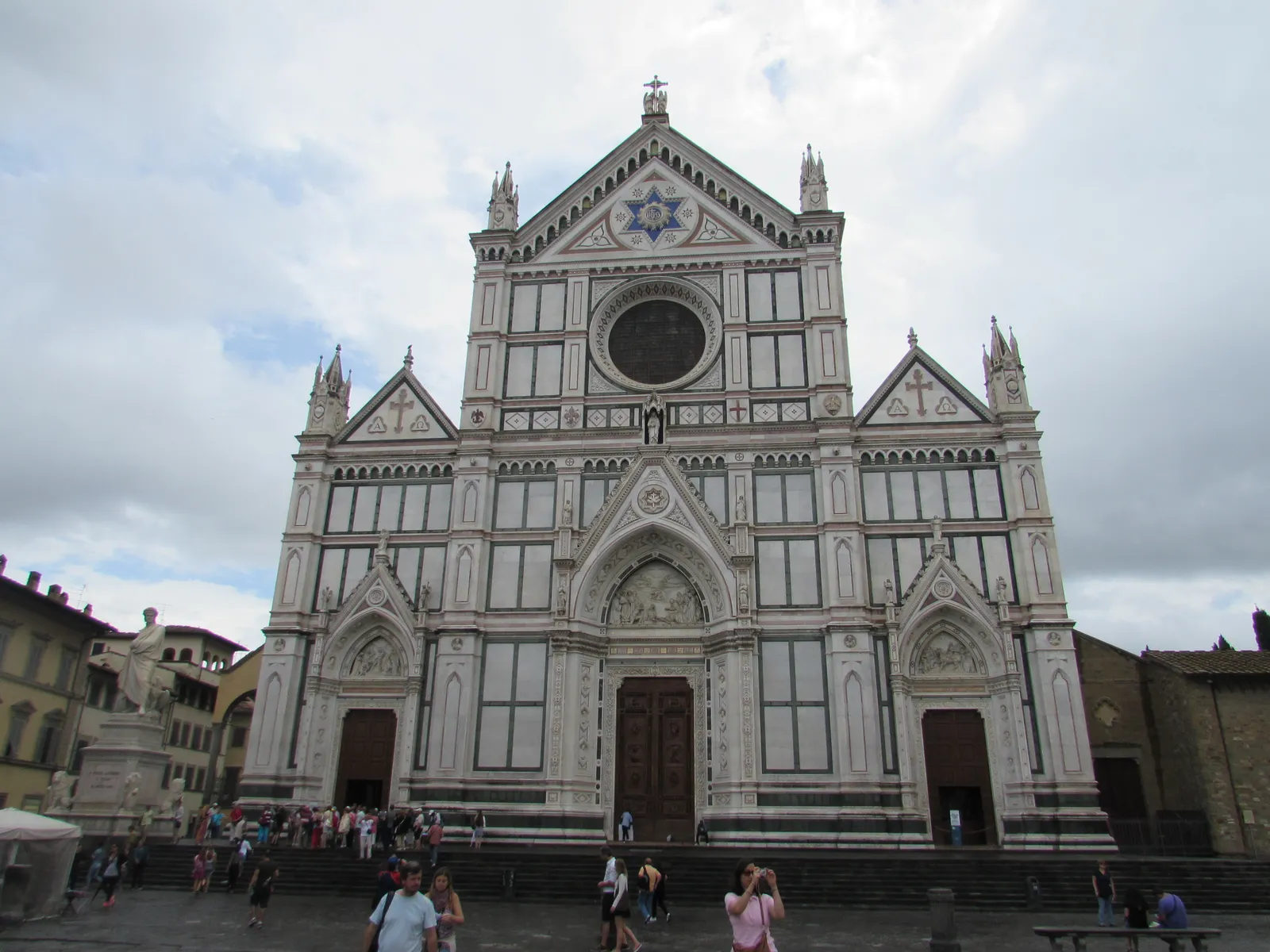 The white, pink, and green marble facade of the Basilica di Santa Croce in Florence with the Dante Alighieri statue in front