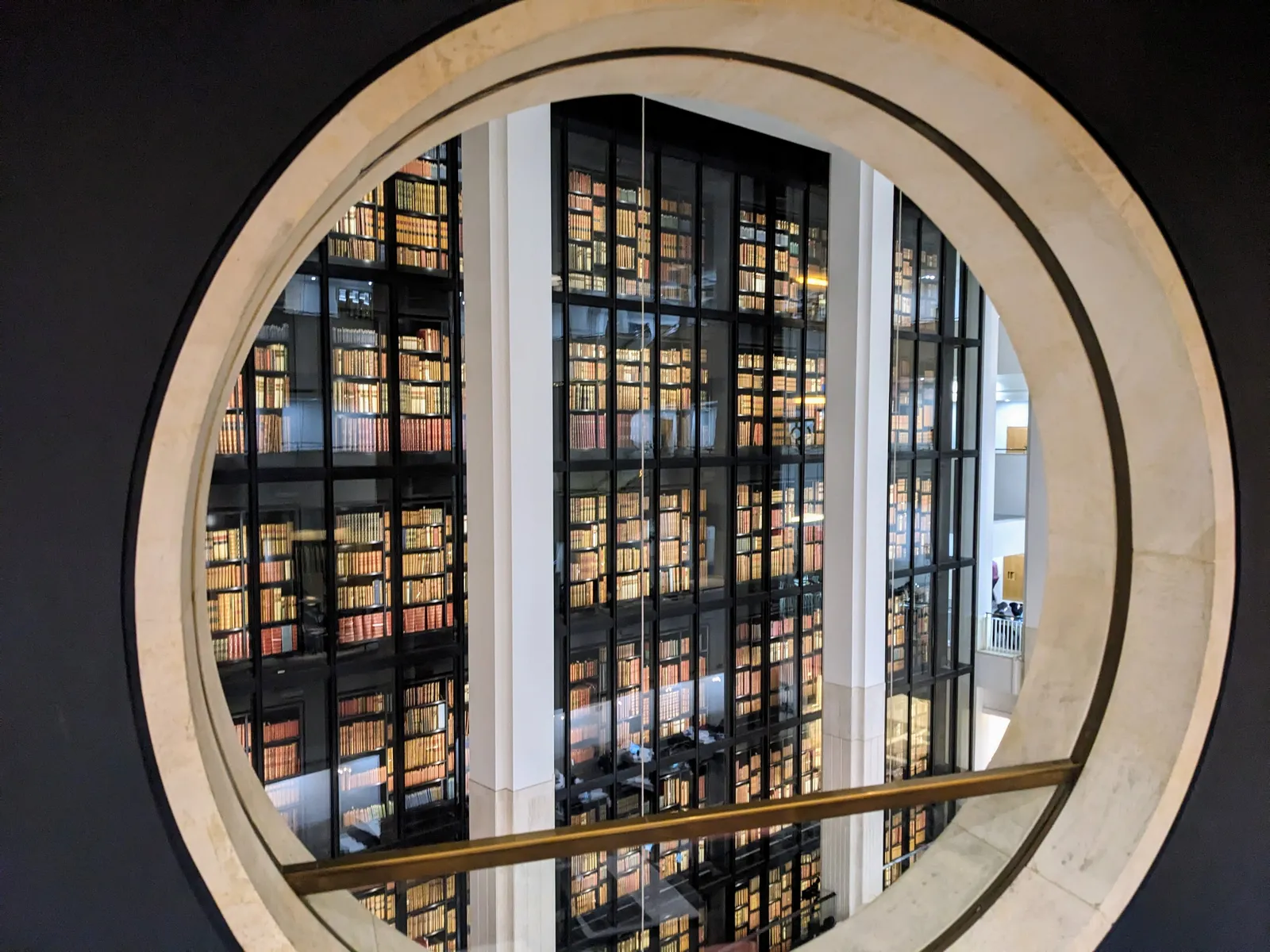 The glass-walled King's Library Tower of leather-bound books seen through a circular window at the British Library