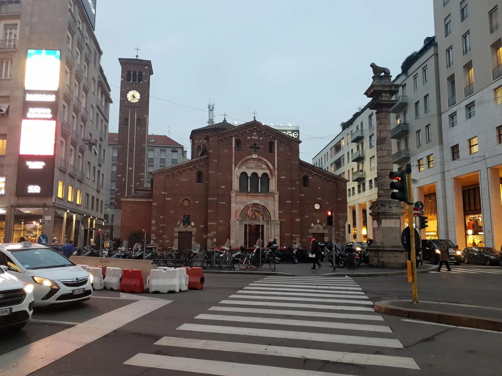 The brick facade and bell tower of the Basilica of San Babila in Milan's Piazza San Babila at dusk