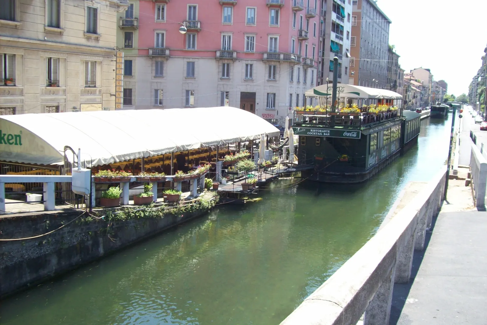 The Naviglio Pavese canal in Milan lined with restaurant boats, canal-side dining, and pastel-colored buildings