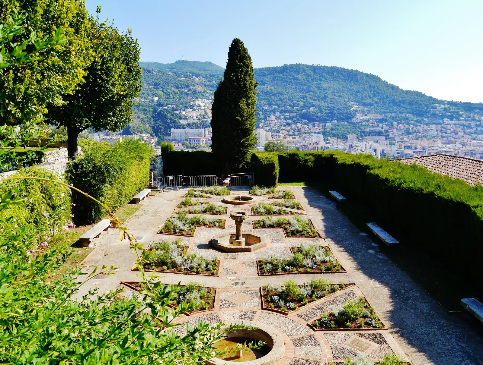 The geometric Italian-style garden of the Cimiez Monastery in Nice, with a stone fountain and a view over the city and hills