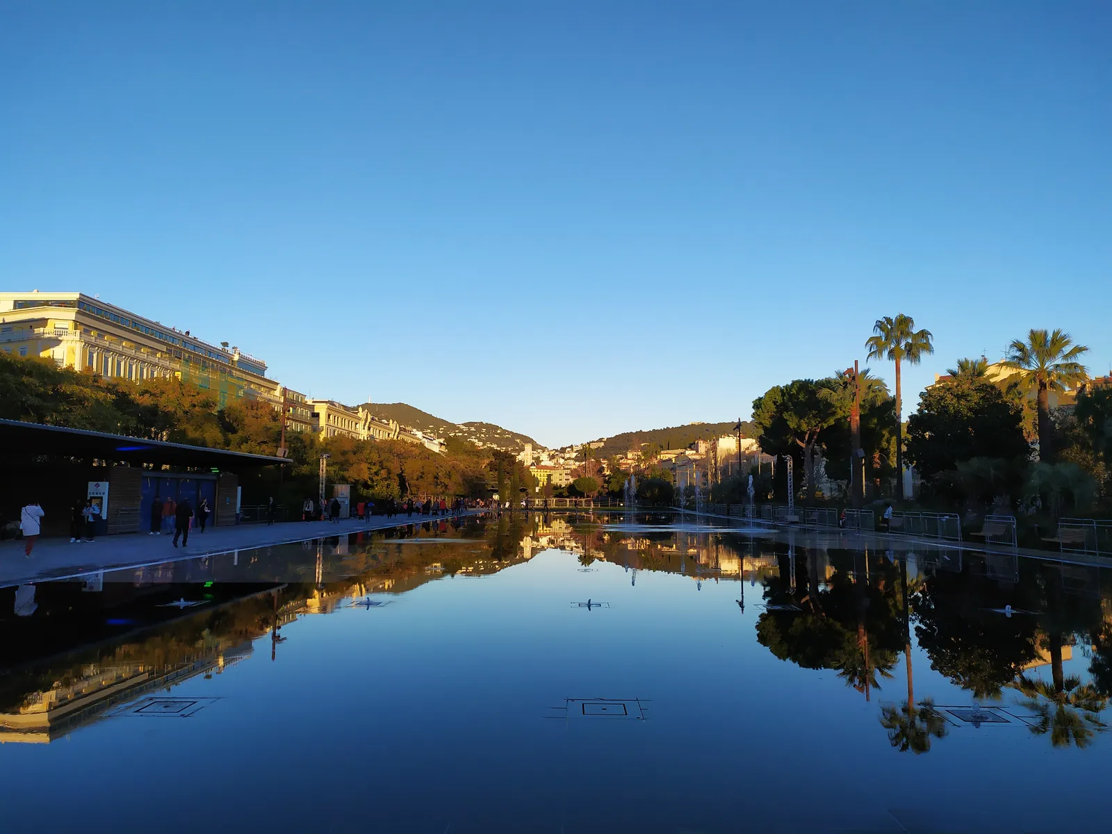 The Miroir d'Eau water mirror at Place Masséna in Nice, reflecting palm trees and buildings at golden hour