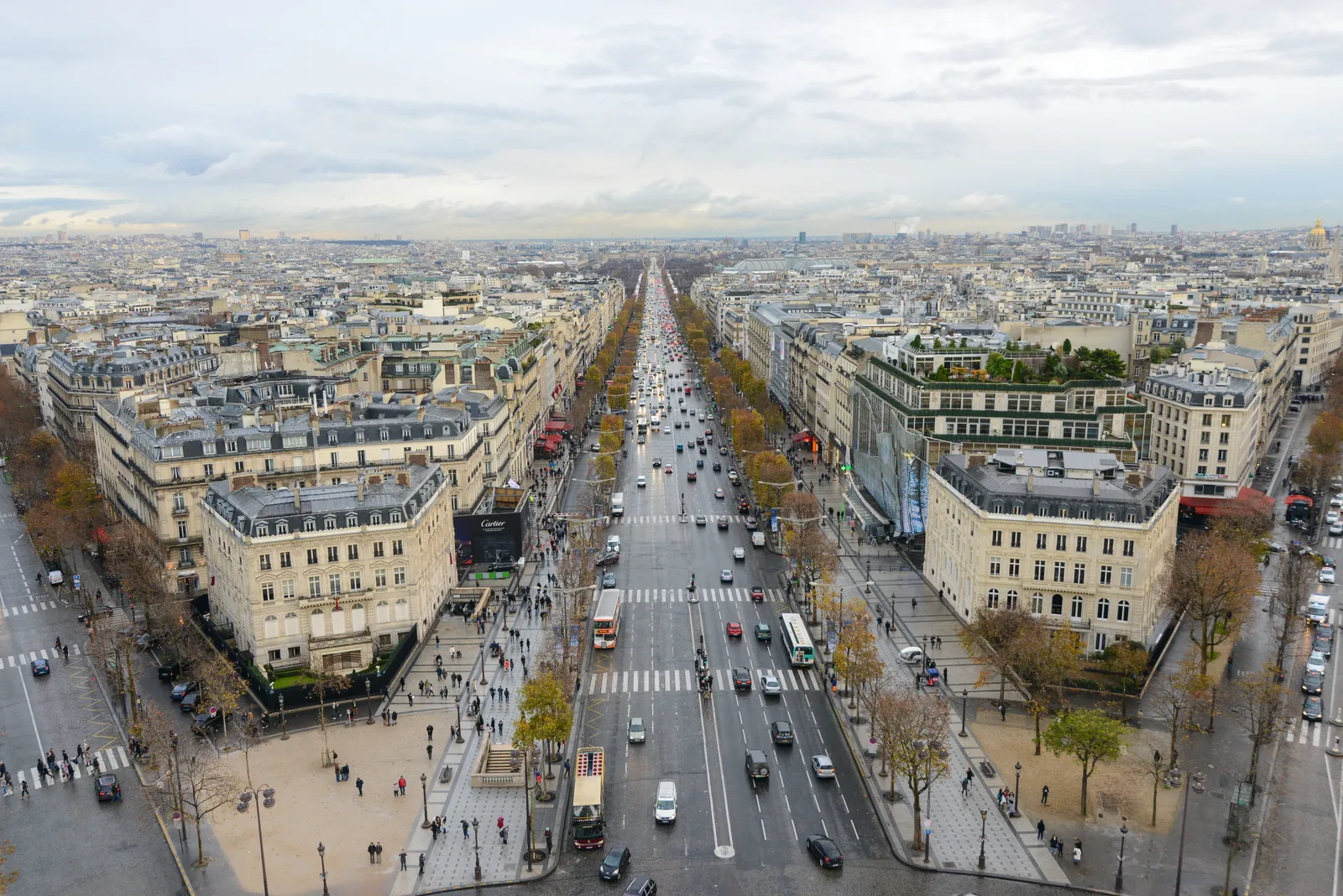 An aerial view down the Avenue des Champs-Élysées from the Arc de Triomphe, lined with buildings, shops, and traffic
