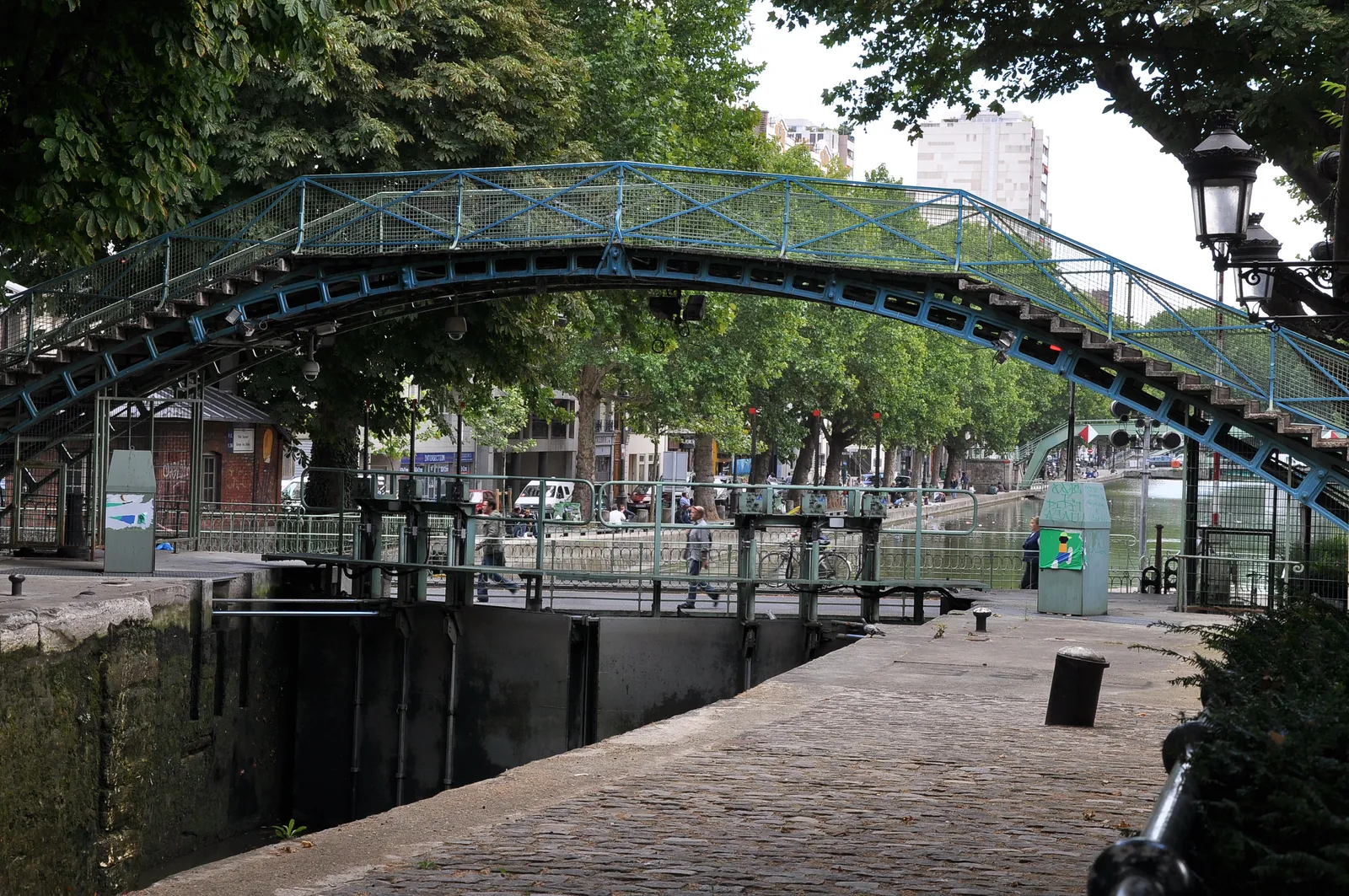 One of Canal Saint-Martin's arched iron footbridges over a lock, with tree-lined quays on either side