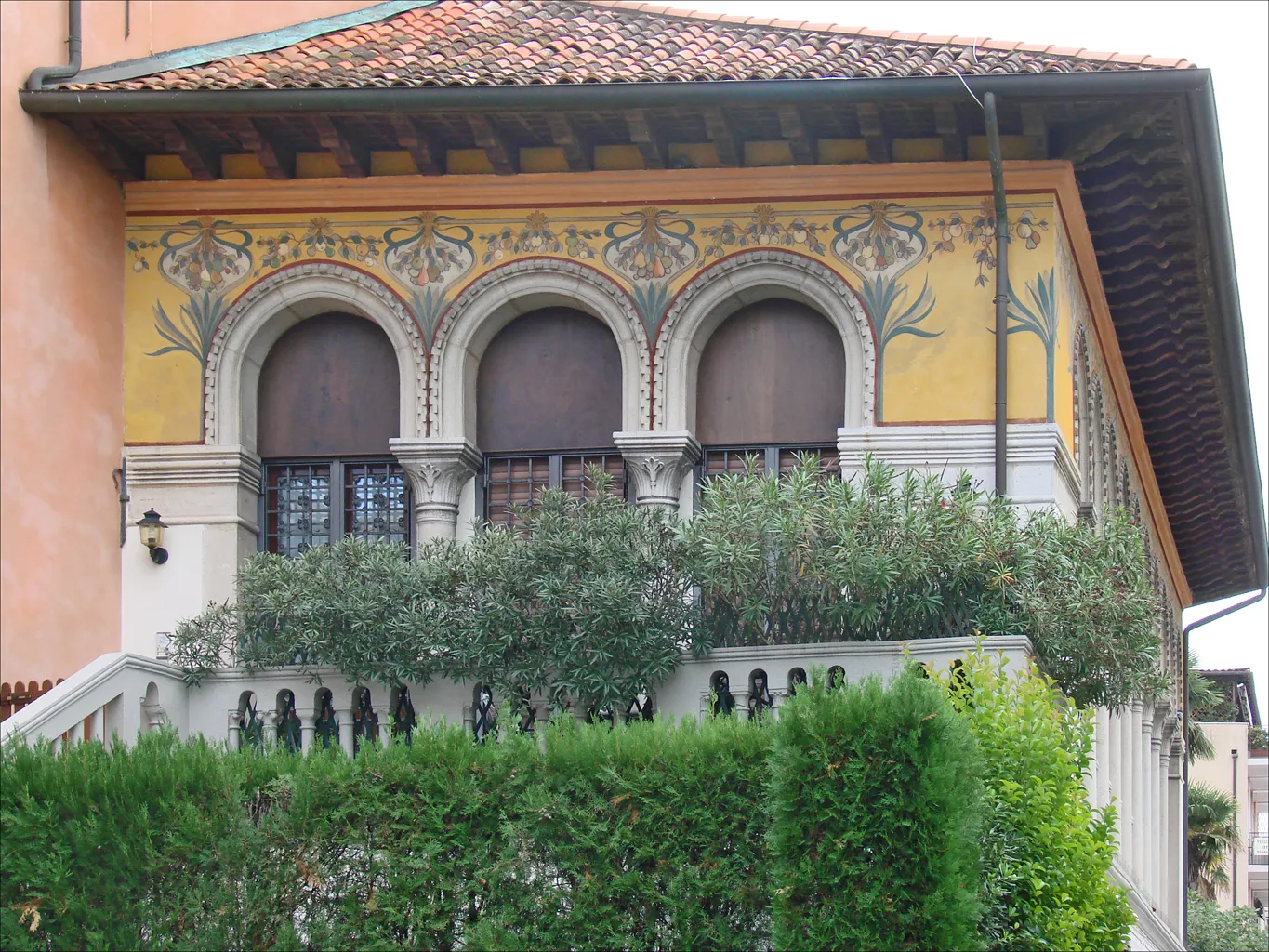 Detail of Villa Otello on the Lido showing three frescoed Liberty-style arched windows above a garden terrace
