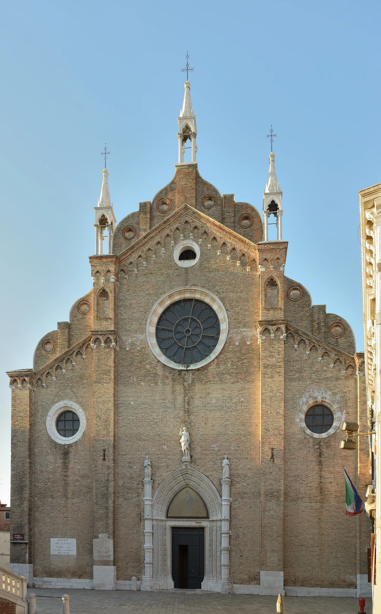 The tall brick Gothic facade of the Basilica dei Frari in Venice with its rose window and stepped roofline