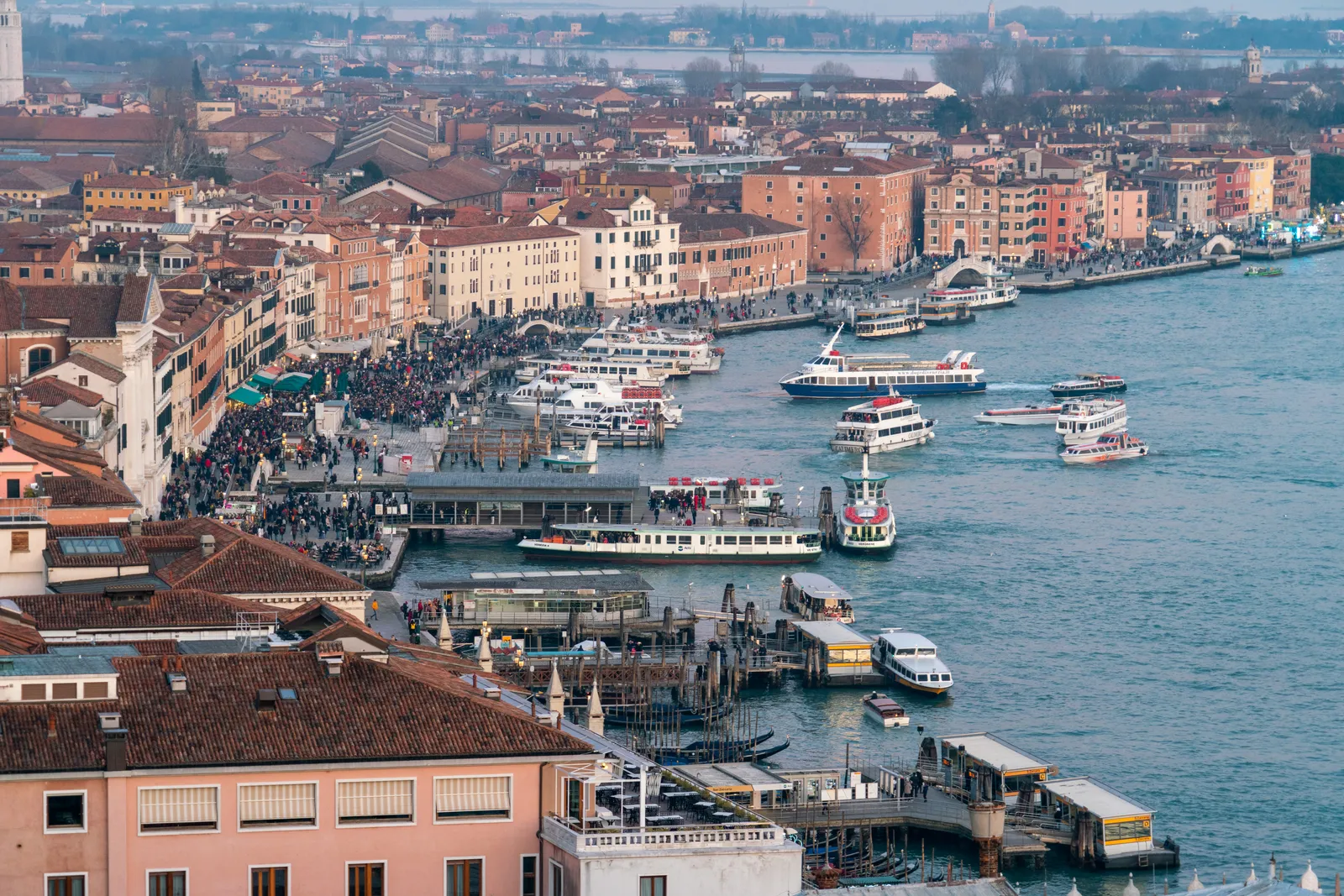 Aerial view of Riva degli Schiavoni in Venice, a wide waterfront promenade crowded with pedestrians and lined with vaporetto docks and moored boats